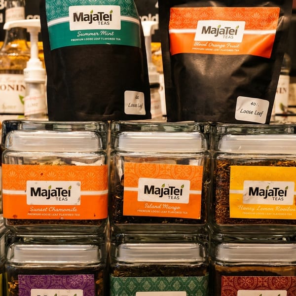 MajaTei loose-leaf tea packages and labeled glass jars displayed on a shelf among Monin syrup bottles.