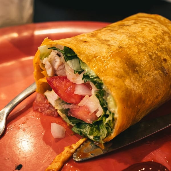 Golden wrap filled with grilled chicken, lettuce, tomato, and onions on a red plate with fork and knife.