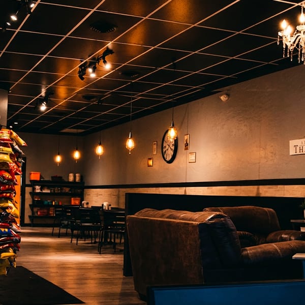 Warmly lit restaurant lounge with chandeliers, pendant lights, leather seating, dessert display case, and colorful packaged snacks.