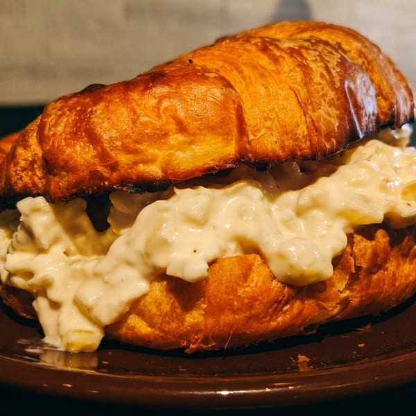 Golden croissant sandwich filled with creamy chicken salad, served on a brown plate.
