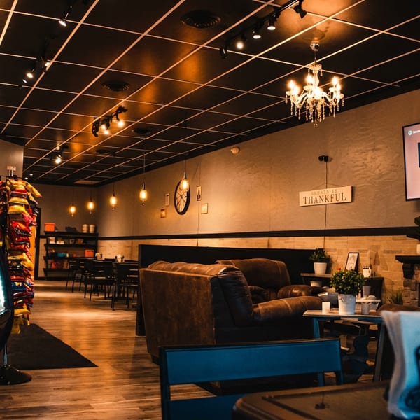 Cozy restaurant lounge with chandeliers, leather seating, dessert display case, fireplace, and wall-mounted television.