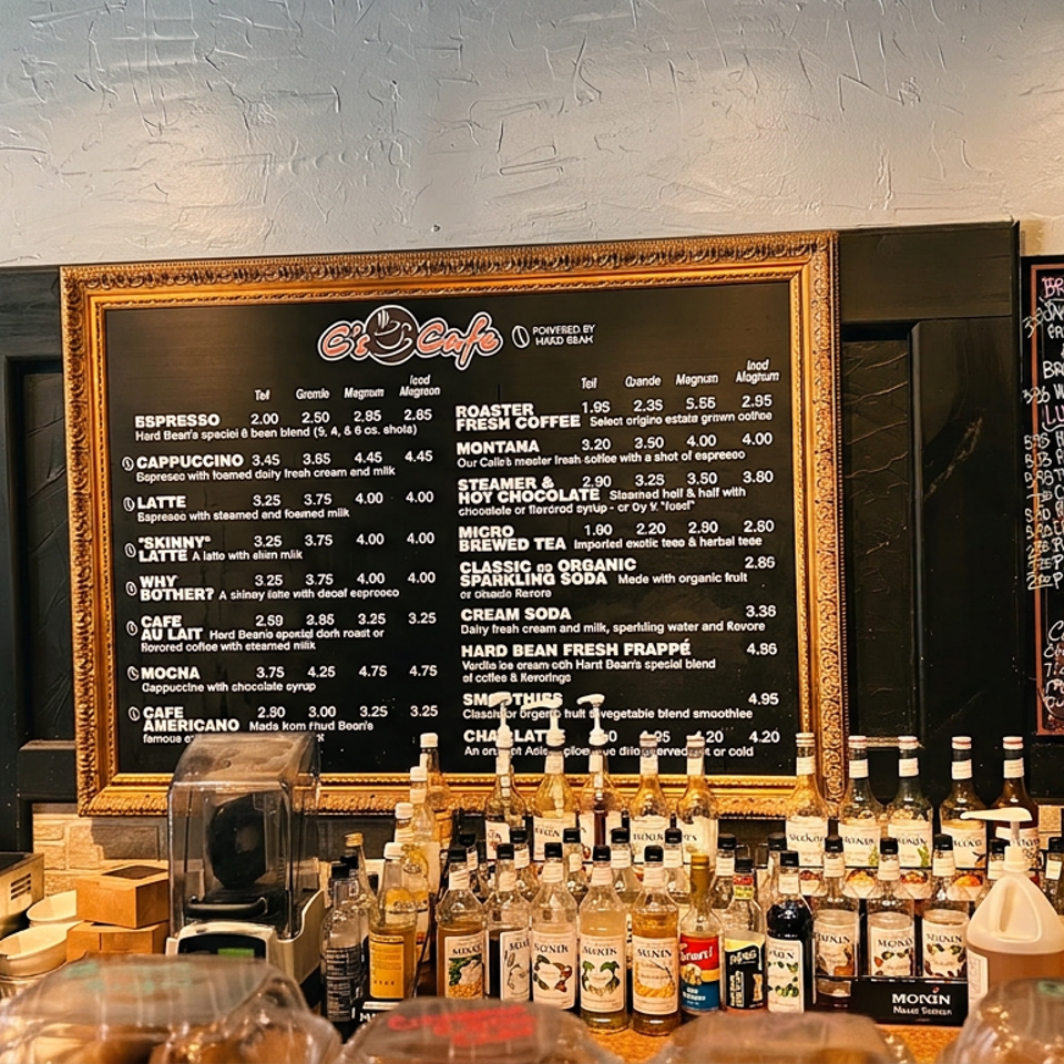 Cafe counter displaying coffee menu boards, syrup bottles, coffee equipment, and pastry containers.